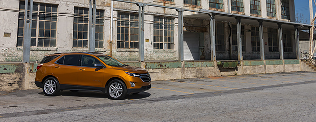 Alt text: A bronze SUV is parked in front of an old, weathered industrial building with peeling paint and large windows, creating a contrast between modern and rustic elements.