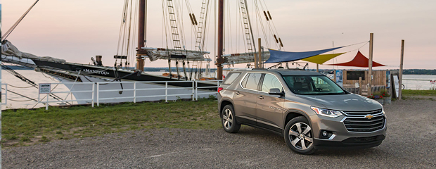 A silver SUV is parked near a marina at sunset, with a large sailboat in the background. The scene conveys a sense of adventure and tranquility.