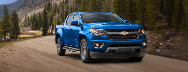 A blue pickup truck drives along a winding dirt road through a forested mountainous area, conveying adventure and rugged reliability.