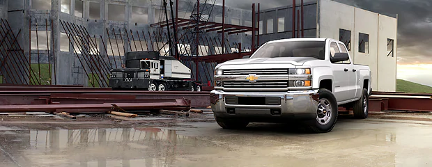 White pickup truck on a construction site with steel beams and machinery in the background. Overcast sky conveys a rugged and industrious tone.