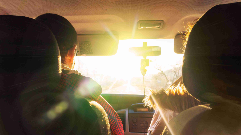 Interior of a car at sunset, with two people sitting in the front seats. The scene is bathed in warm sunlight, creating a calm, serene atmosphere.
