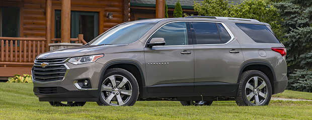 A silver SUV is parked on a grassy area in front of a wooden cabin. The vehicle is sleek and modern, conveying a sense of adventure and comfort.