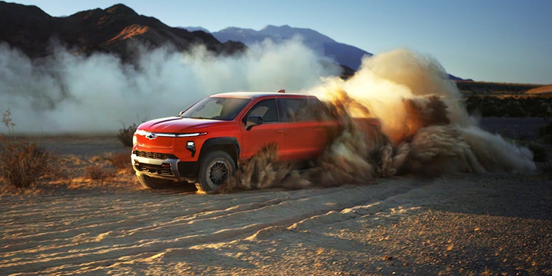 A 2026 Silverado EV Trail Boss driving through a vast desert landscape under a clear blue sky.