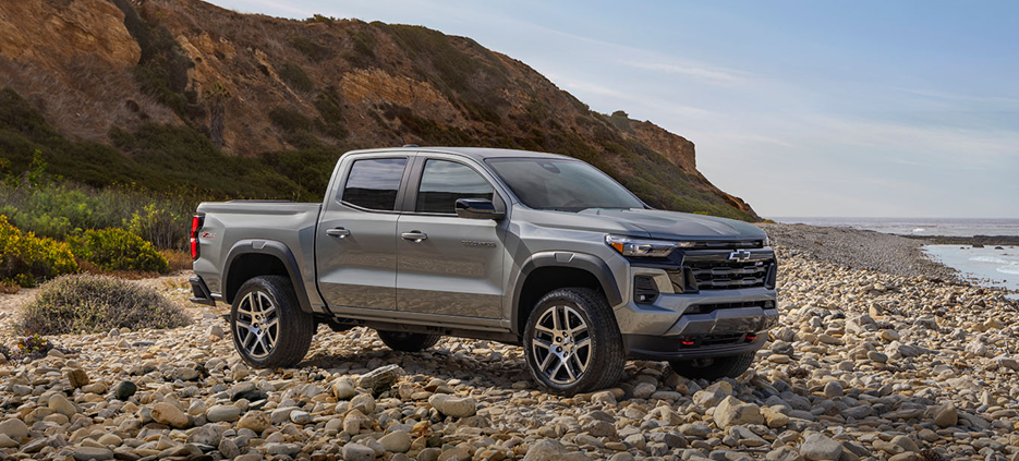 2025 Chevrolet Colorado gray midsize pickup truck parked on a rocky coastal landscape, showcasing its rugged off-road stance