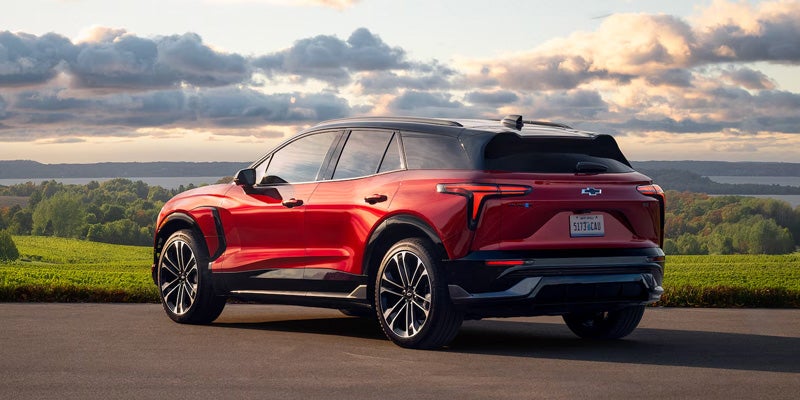 A sleek red Blazer EV parks on a rural road with scenic green fields and a cloudy sky in the background, conveying a sense of adventure and freedom.