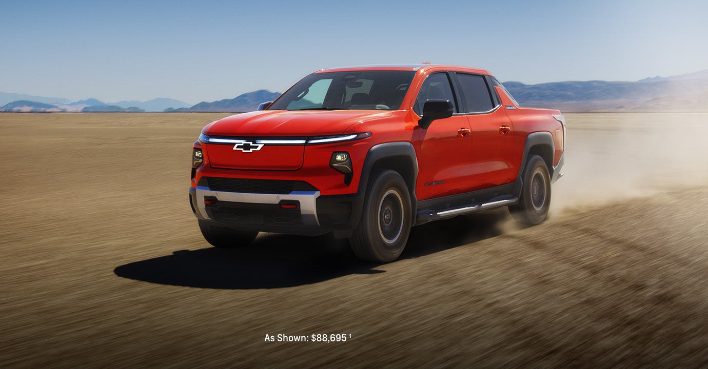 2026 Chevrolet Silverado EV pickup truck in red driving across a wide desert landscape with mountains in the background.