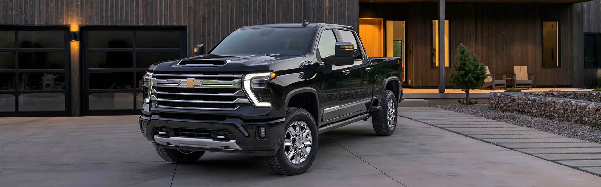 2026 Chevrolet Silverado HD in black parked outside a modern home with illuminated garage doors.