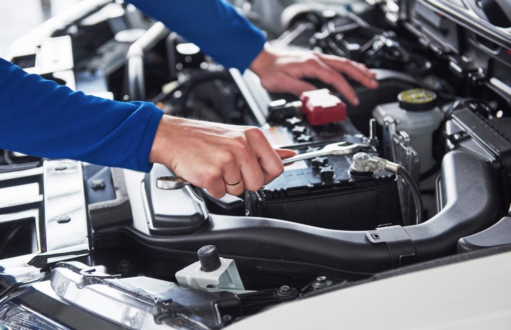 Mechanic using a wrench to tighten a car battery connection under the hood.