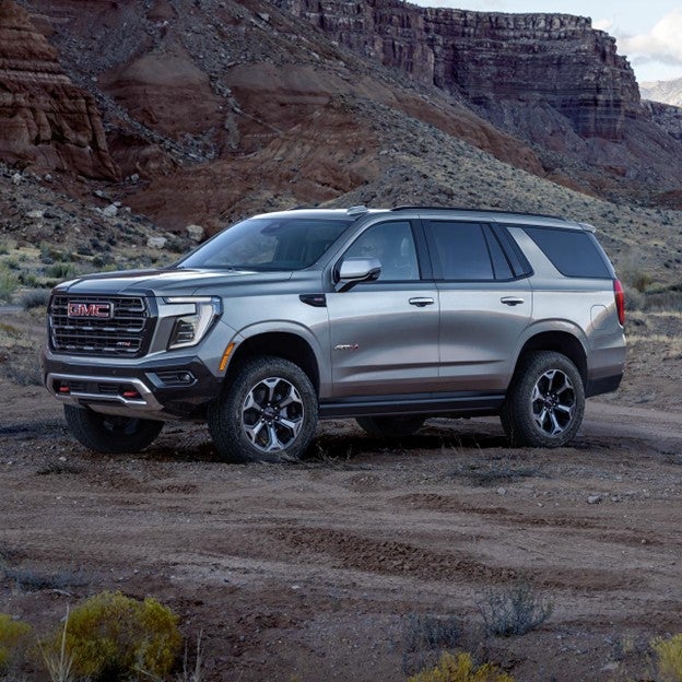 2025 GMC Yukon XL AT4 full-size SUV parked off-road in rugged desert terrain near red rock cliffs.
