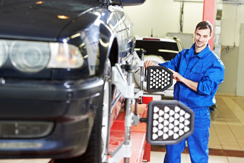 A mechanic performing a tire alignment on a car in a workshop.