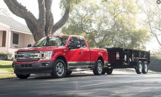 Red Ford F-150 pulling a black trailer in front of a home