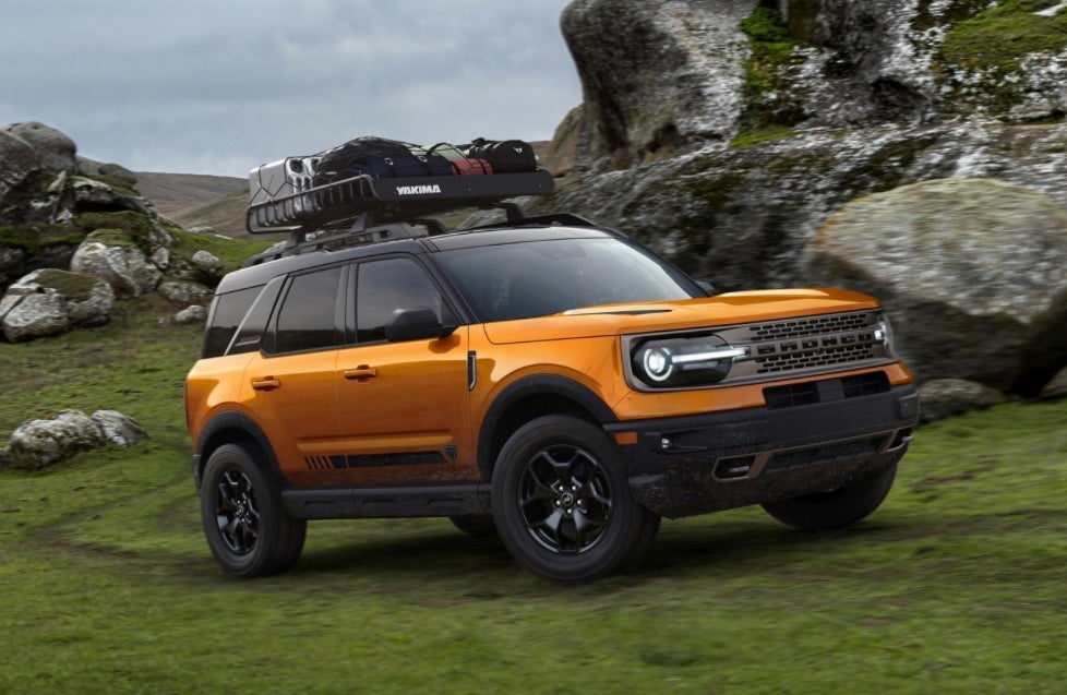 Orange Ford Bronco with luggage in roof driving off road