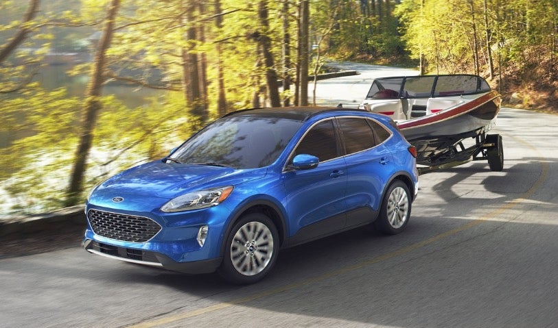 Blue Ford Escape pulling a boat on a trailer to a lake