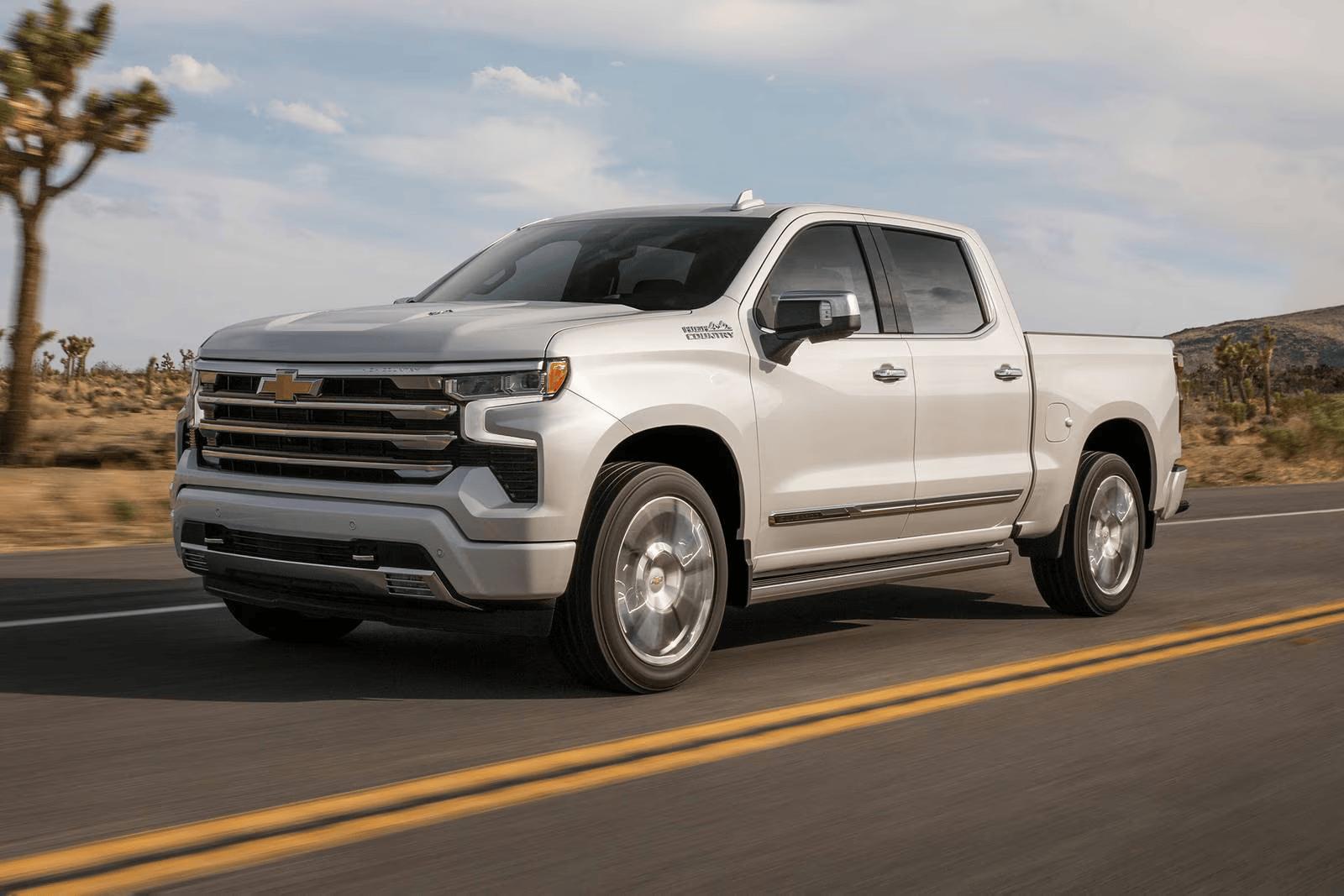 Light-colored Chevrolet Silverado pickup truck driving on a desert road.