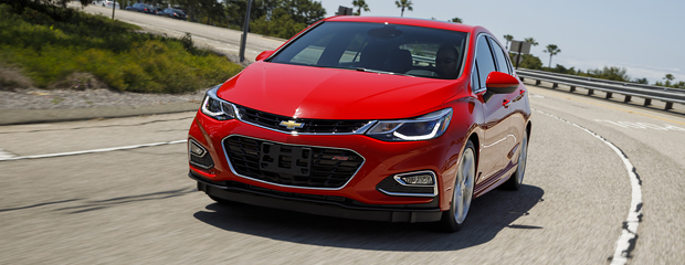 A sleek red sedan with a Chevrolet logo drives on a sunny, curving highway. The car's design is modern and dynamic, conveying a sense of speed and style.