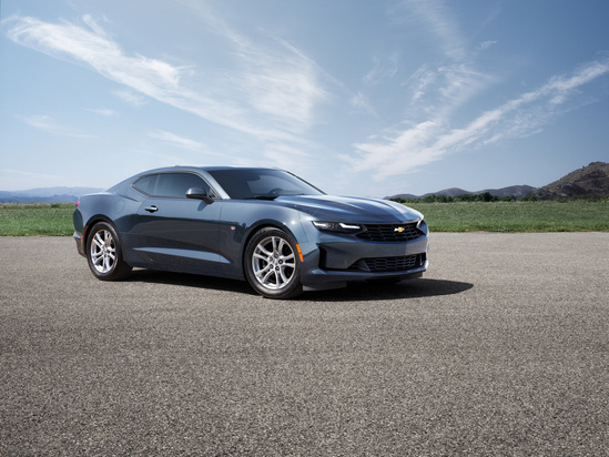 A sleek, modern gray sports car is parked on an empty paved road. The backdrop features a clear blue sky and distant mountains, conveying a sense of freedom and power.