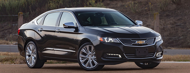 A sleek black sedan with a Chevrolet logo on the grille is parked on a road. The background features grassy terrain, conveying a calm, elegant atmosphere.