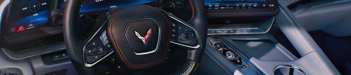A close-up of the steering wheel and dashboard in a Corvette, showcasing the distinctive logo, controls, and sleek interior design