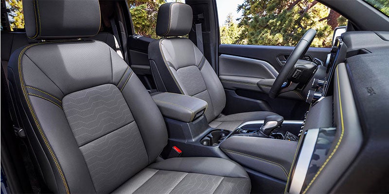 Interior view of the 2025 Chevy Colorado, angled from the front passenger side. The image shows the driver’s seat, steering wheel, and scenic forest views through the windows on a sunny day near JK Chevrolet.