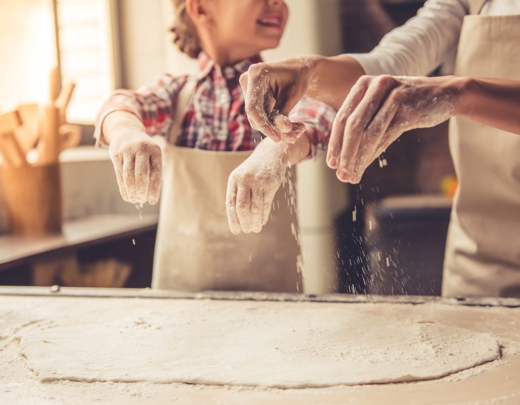 little girl and her mother are sprinkling the dough with flour and smiling while baking