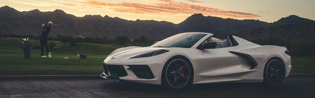 A white 2025 Corvette Stingray parked beside a golf course at sunset, with a golfer swinging in the background near Turner Chevrolet.