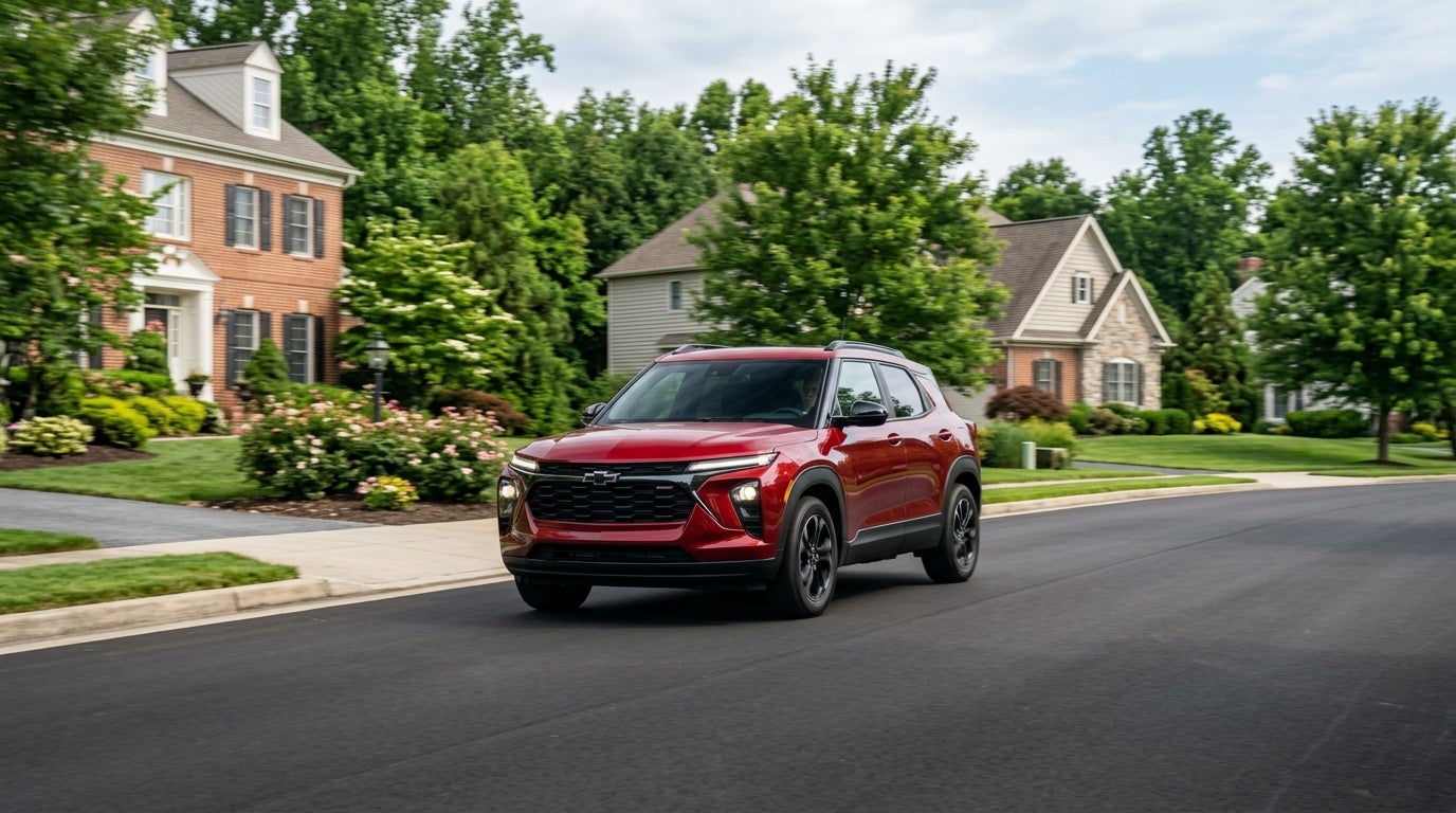 A red Chevrolet Trax SUV driving down a tree-lined suburban street past large family homes. (Representative image for illustration purposes only. Actual vehicle may vary based on trim and configuration.)