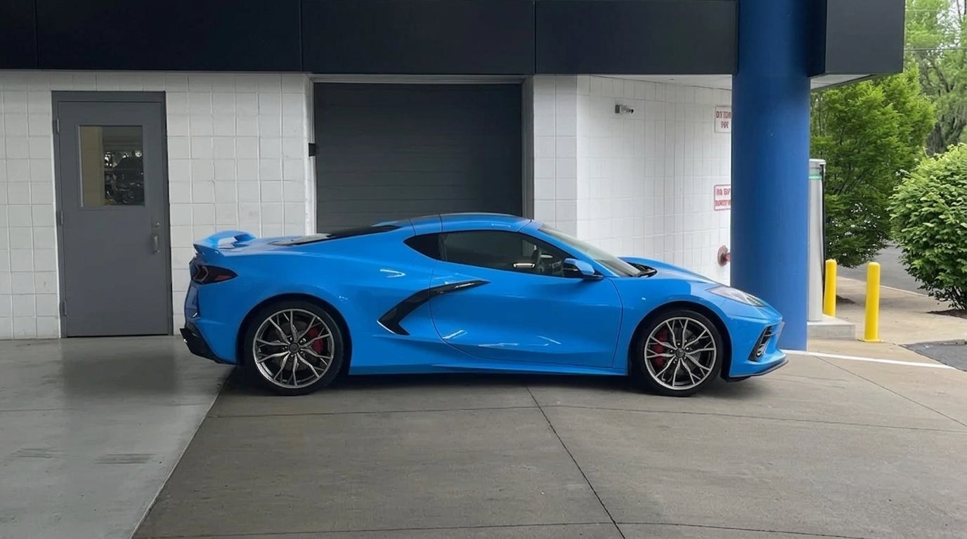 A bright blue Chevrolet Corvette C8 sports car parked outside a building with white brick walls. (Representative image for illustration purposes only. Actual vehicle may vary based on trim and configuration.)