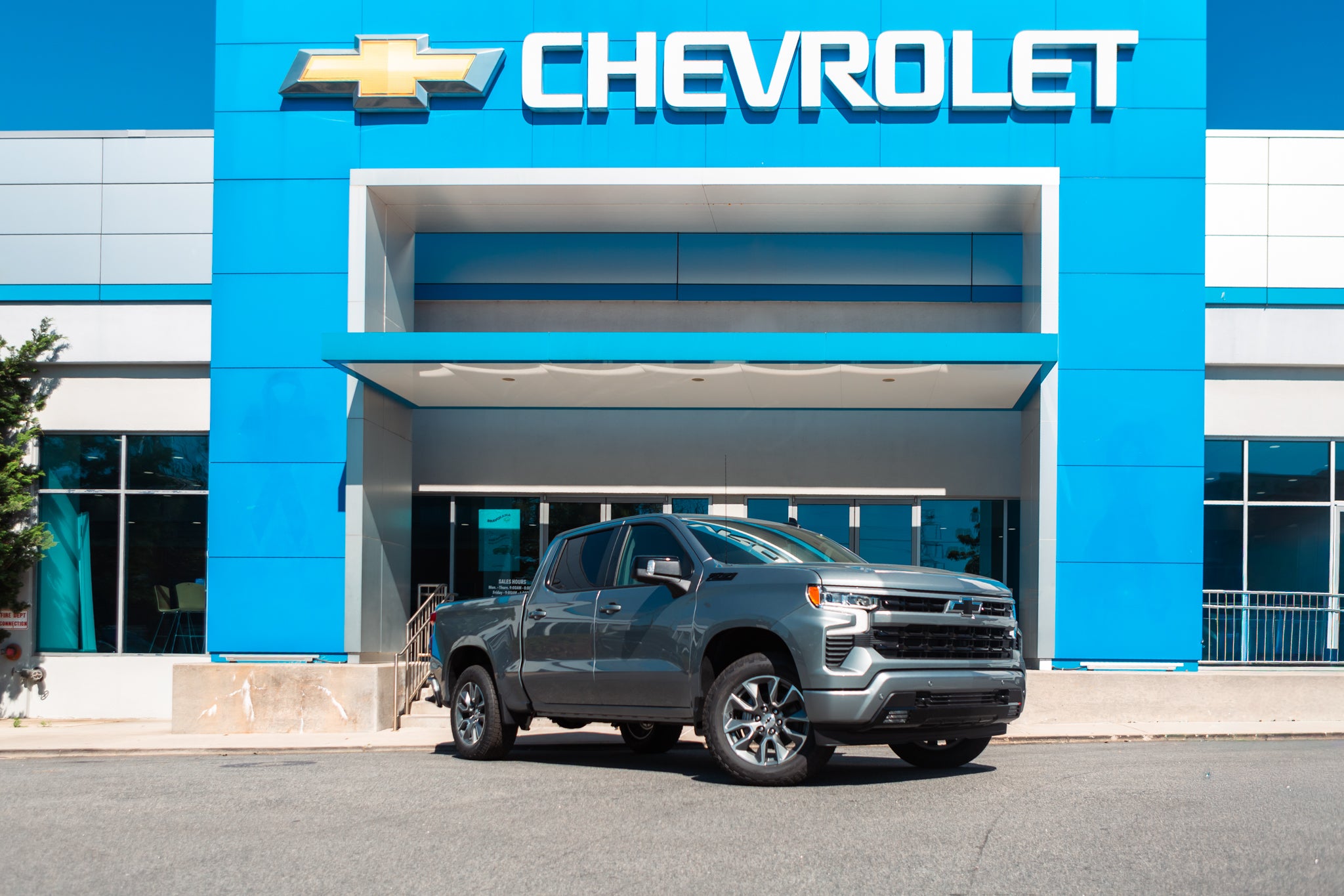 A gray Chevrolet Silverado pickup truck parked in front of a blue Chevrolet dealership building.