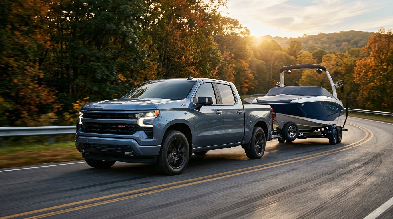 Slate blue pickup truck towing a speedboat on a trailer along a winding road surrounded by autumn trees. (Representative image for illustration purposes only. Actual vehicle may vary based on trim and configuration.)