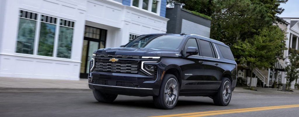 A blue 2025 Chevy Suburban driving down a city street.