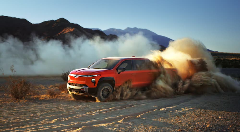 A red 2025 Chevy Silverado EV driving through a desert.
