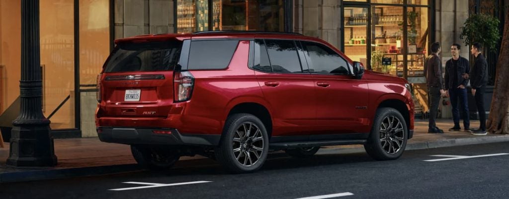 A 2023 red Chevy Tahoe parked on a city street by a shop.