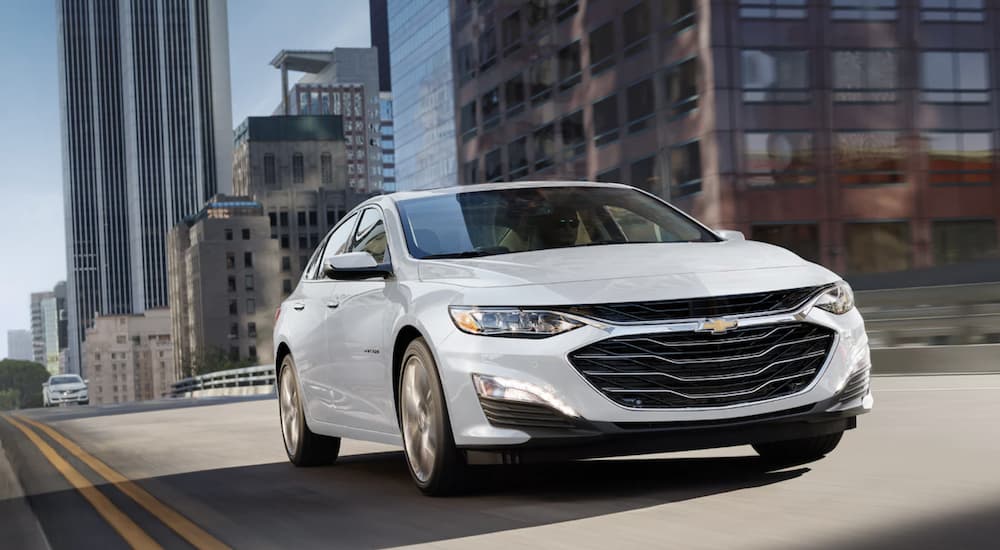 A white 2022 Chevy Malibu driving in a city.
