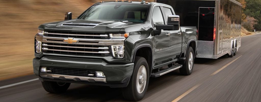 A black 2023 Chevy Silverado 2500HD High Country towing a trailer after viewing work trucks for sale.