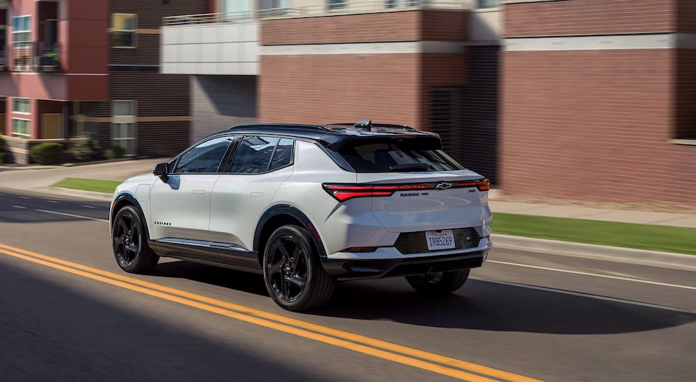 Rear view of a white 2025 Chevy Equinox EV driving through a city.