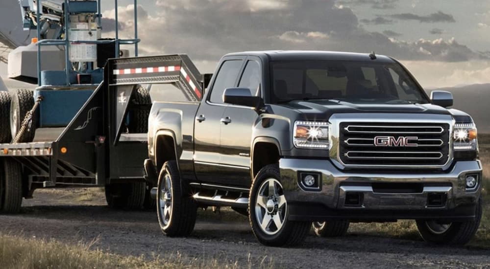 Black 2015 GMC Sierra 2500HD towing heavy machinery on a trailer.