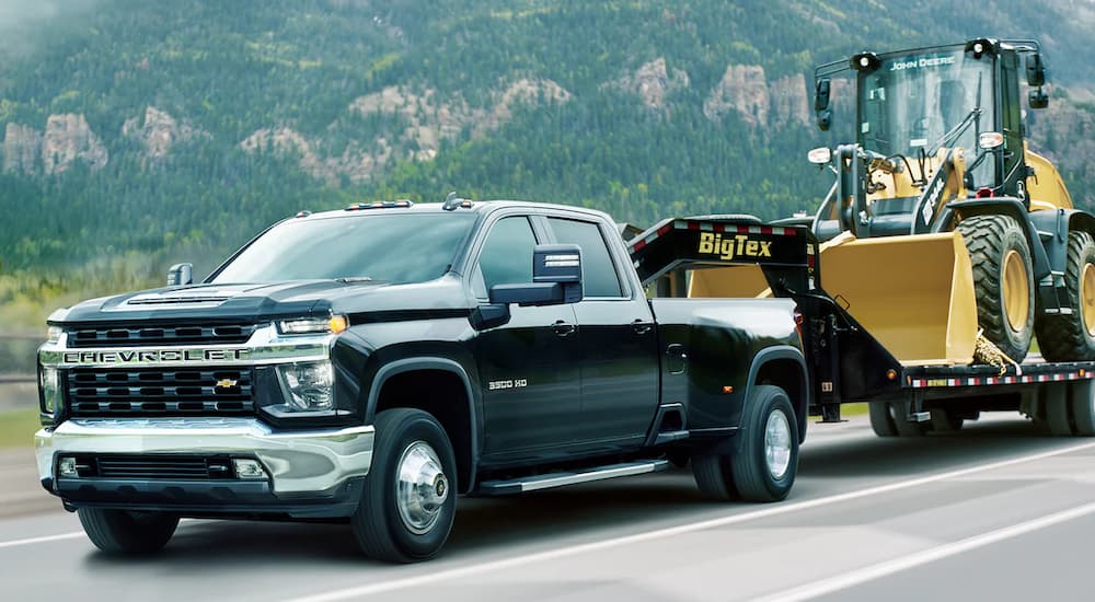 Black 2021 Chevy Silverado 3500HD towing heavy machinery on a trailer.