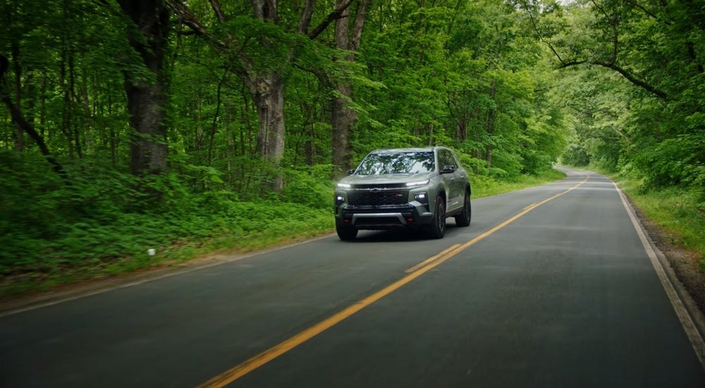 A grey 2025 Chevy Traverse for sale ear San Antonio driving on a tree-lined road.