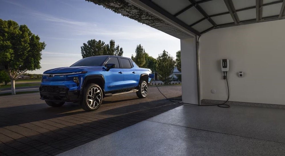 A blue 2024 Chevy Silverado EV RST parked near a garage.