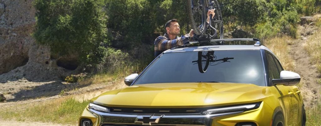 Man taking a bike off the top of a yellow 2024 Chevy Trailblazer.