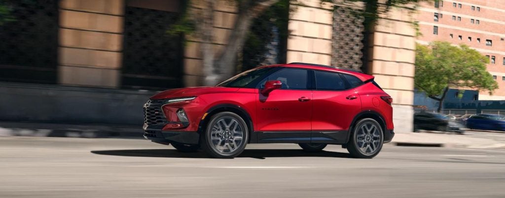 Side view of a red 2024 Chevy Blazer RS driving down a street.