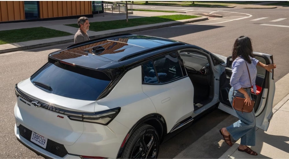 People exiting a white 2025 Chevy Equinox EV RS.