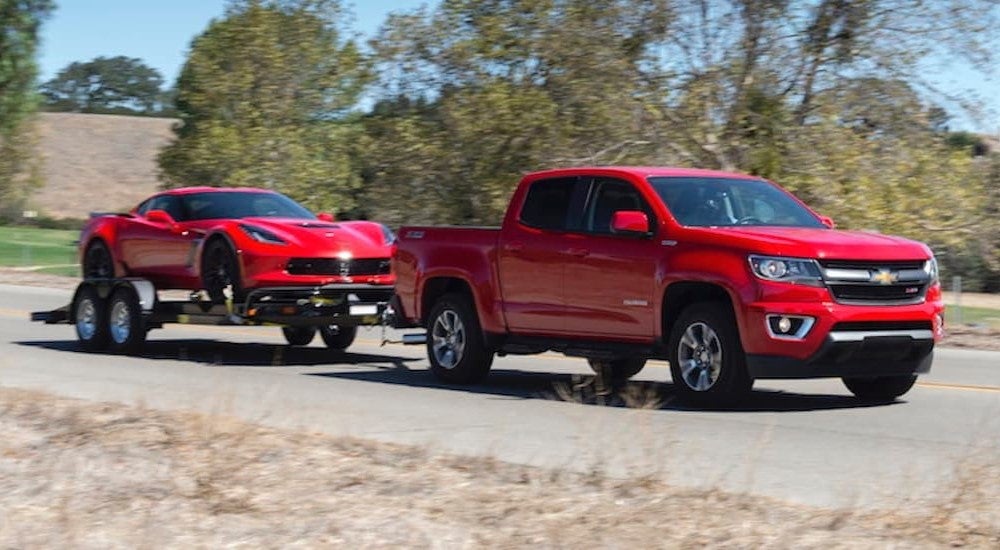A red 2018 Chevy Colorado towing a red Corvette to a used truck dealership.