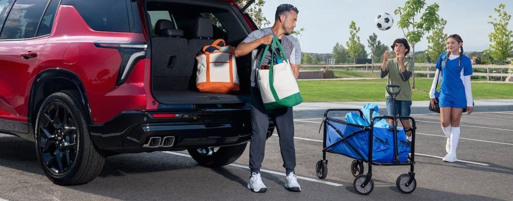 Father packing bags into the back of a red Chevy Traverse.