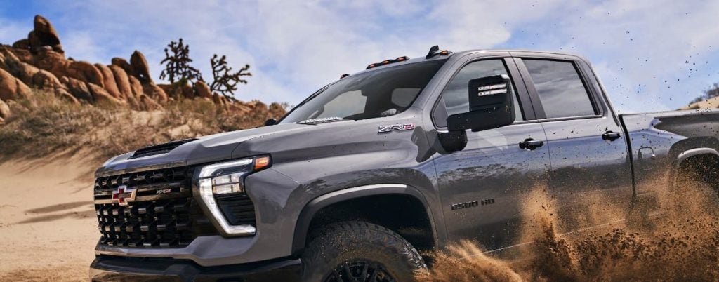 A silver Chevy Silverado 2500 HD driving through mud.