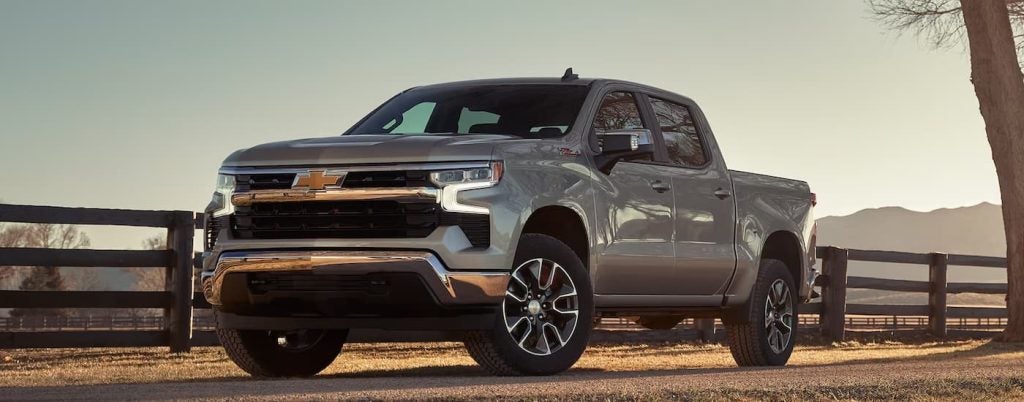 A silver 2024 Chevy Silverado 1500 LT parked beside a ranch.