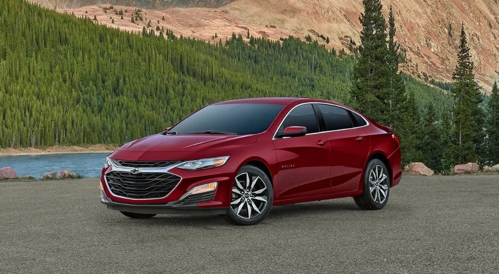 A red 2022 Chevy Malibu parked near a lake and trees.