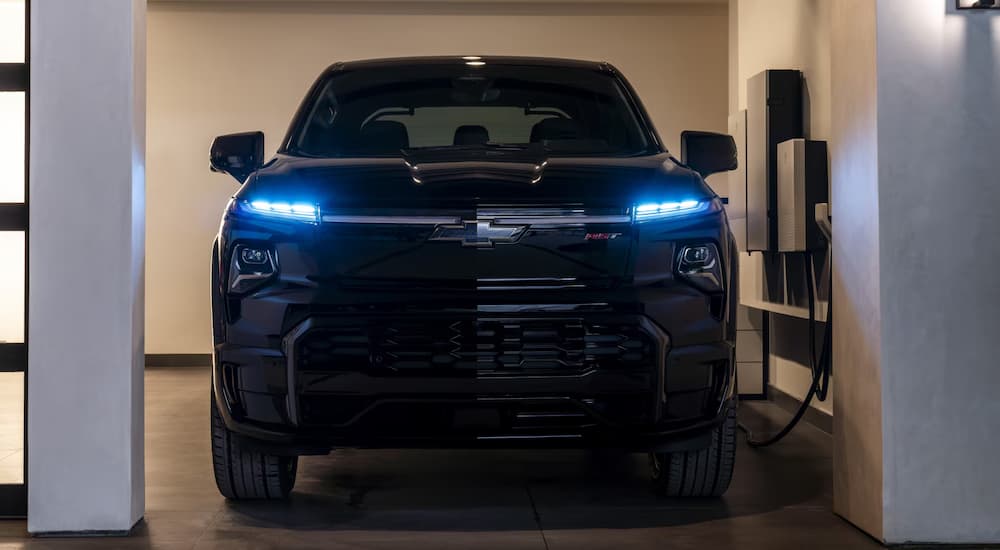 A black 2025 Chevy Silverado EV plugged in and charging while parked in a garage.