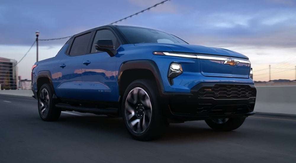 A blue 2024 Chevy Silverado EV driving at dusk.
