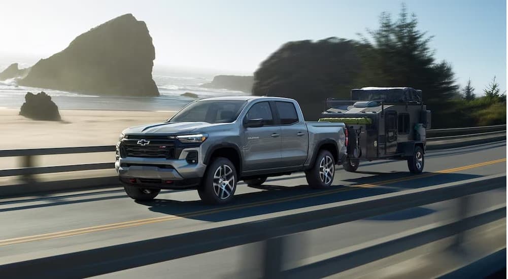 A silver 2024 Chevy Colorado Z71 towing a trailer near water.